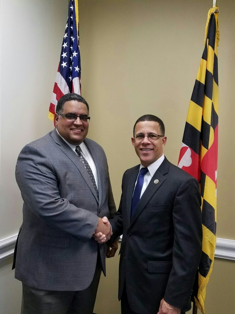 Two men shake hands in front of the U.S. and Maryland flags as VFI leaders meet Members of Congress during National Entrepreneurship Week.